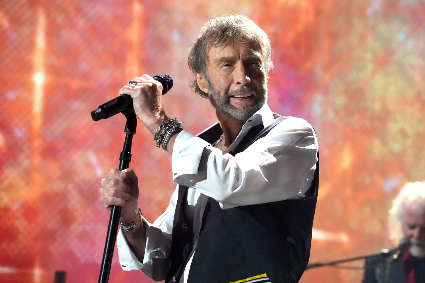 Paul Rodgers nie wystąpi z Bad Company na gali Rock and Roll Hall of Fame Mężczyzna z mikrofonem w dłoni na scenie podczas koncertu, ubrany elegancko w koszulę i kamizelkę, w tle rozmyte kolorowe światła dodające atmosfery występowi.