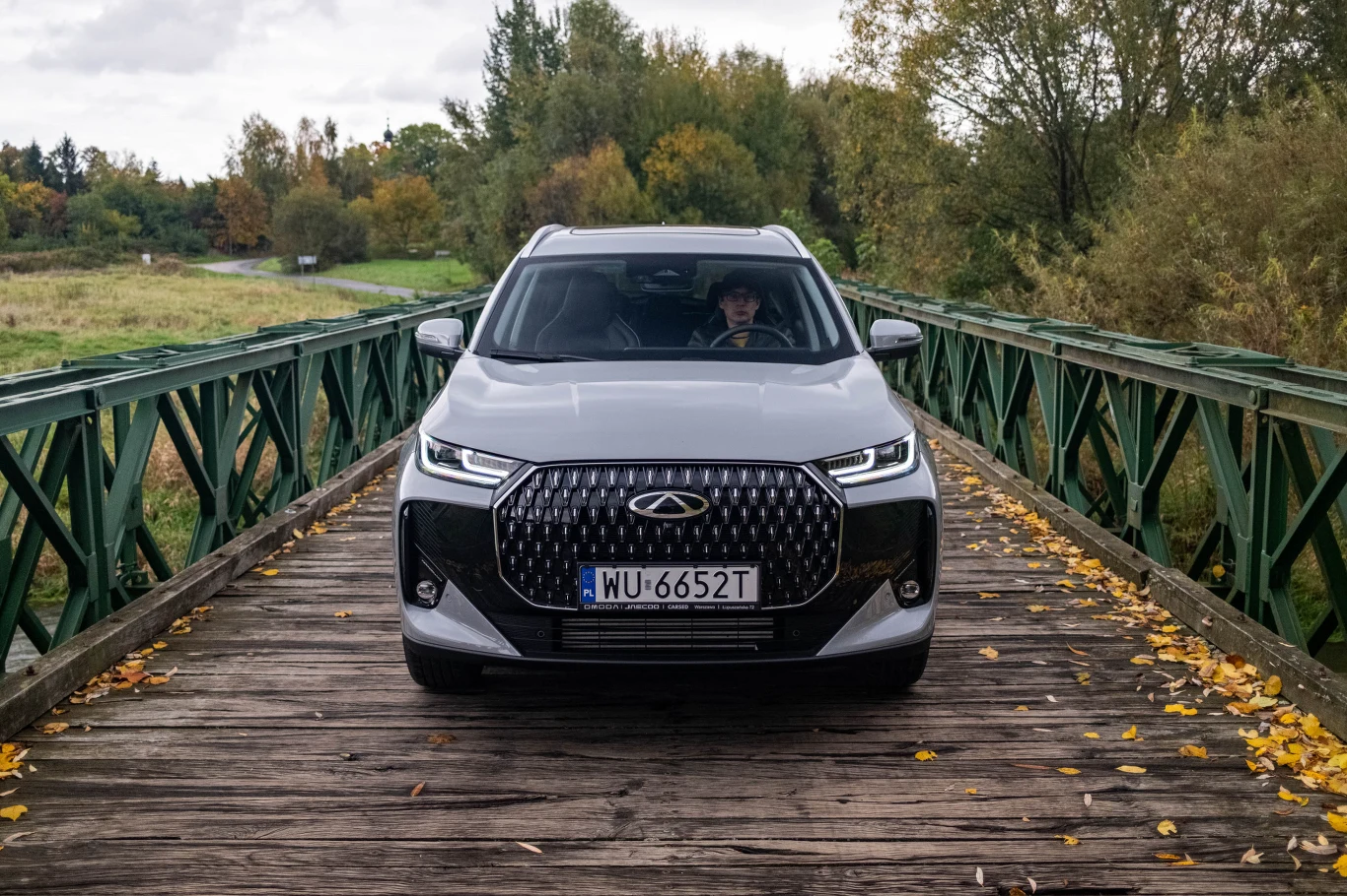 Przód auta zdominowany jest przez ogromną osłonę chłodnicy. Całość jest spójna, ale mało oryginalna. Nowoczesny srebrny samochód osobowy o charakterystycznym przednim grillu, stojący na drewnianym moście z metalowymi barierkami, otoczony jesienną przyrodą i liśćmi na deskach mostu.