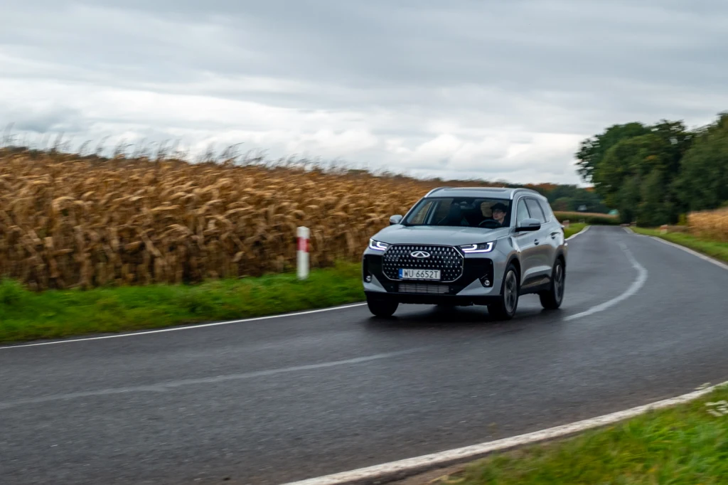Na krętych drogach układ kierowniczy nie pozwala czerpać radości z jazdy, a jedynie “trafiać” samochodem w drogę. Srebrny samochód marki Audi jedzie po asfaltowej, krętej drodze otoczonej polami kukurydzy, w tle widoczne chmury i zieleń drzew.