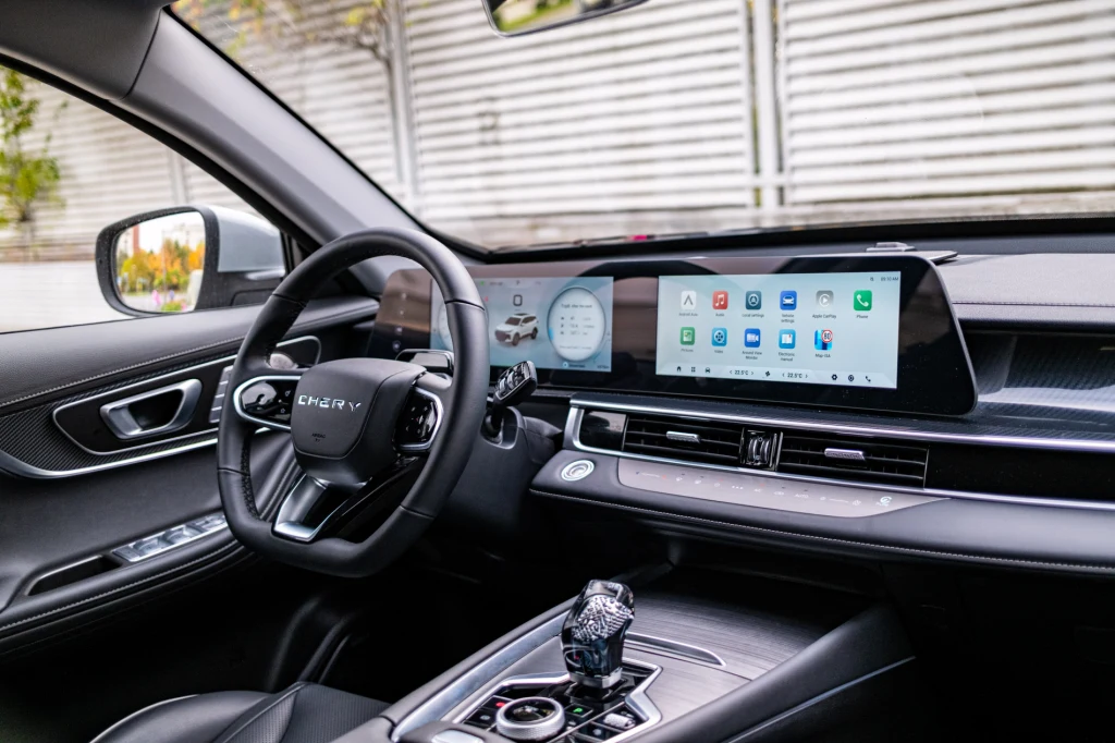 Jakość spasowania kabiny i materiałów jest, żeby nie przesadzić, bardzo dobra. Panel pod ekranem pozwala sterować klimatyzacją, ale wzrok i tak trzeba opuścić. Nowoczesne wnętrze samochodu z dużym, panoramicznym ekranem centralnym i systemem multimedialnym, skórzaną kierownicą oraz estetycznym wykończeniem. Na konsoli środkowej znajduje się selektor biegów, a na ekranie widoczny jest interfejs pokładowy