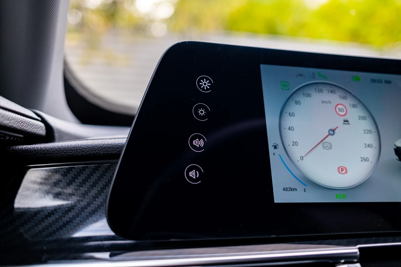 Z lewej strony cyfrowych zegarów znalazły się pola do sterowania ich jasnością oraz… poziomem głośności kierunkowskazów. Elektroniczny wyświetlacz na desce rozdzielczej samochodu, z widocznym wskaźnikiem prędkości i poziomu baterii, otoczony jasnym wnętrzem oraz nowoczesnymi ikonami ustawień po lewej stronie ekranu.