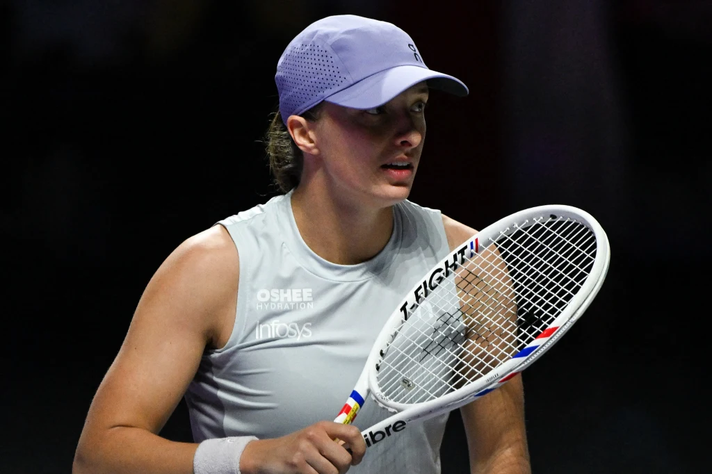 Iga Świątek podczas WTA Finals 2025 Tenisistka w jasnej koszulce sportowej i czapce z daszkiem trzymająca rakietę tenisową, przygotowująca się do gry na korcie podczas rozgrywek sportowych.