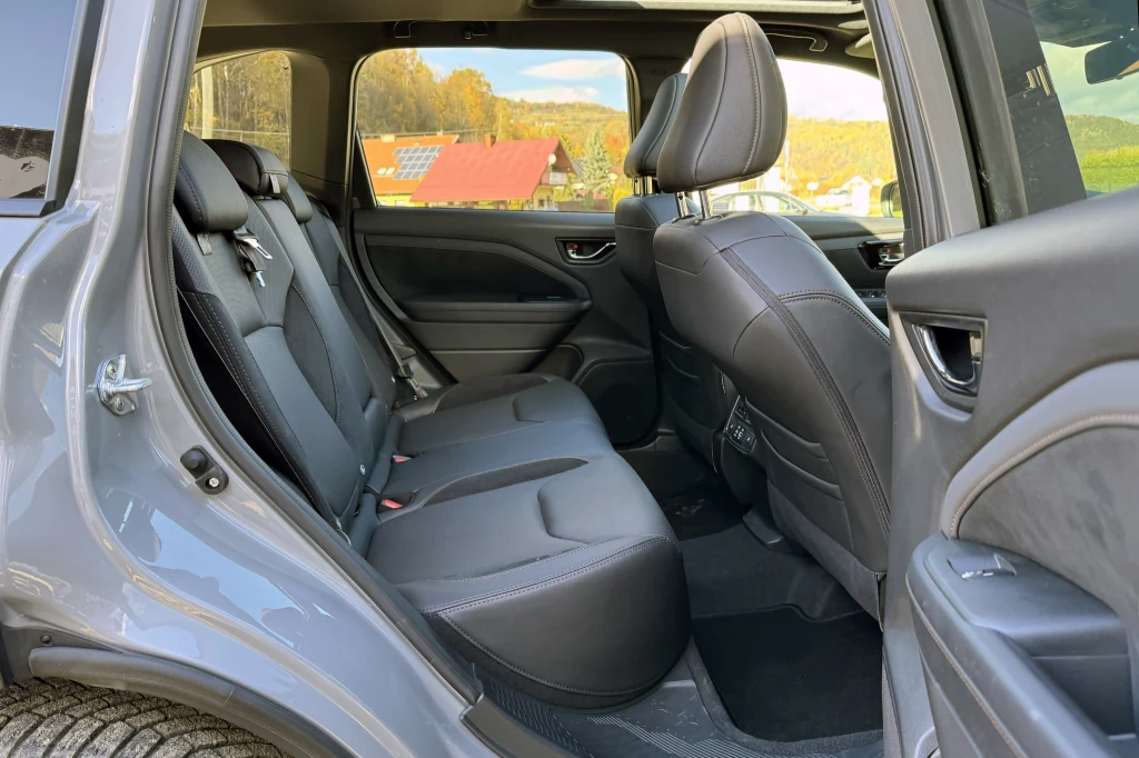 Wnętrze samochodu osobowego z czarną tapicerką, widoczny tylny rząd siedzeń i fragment przedniego fotela, na tle lekko rozmytego widoku przez okno tyłu samochodu.