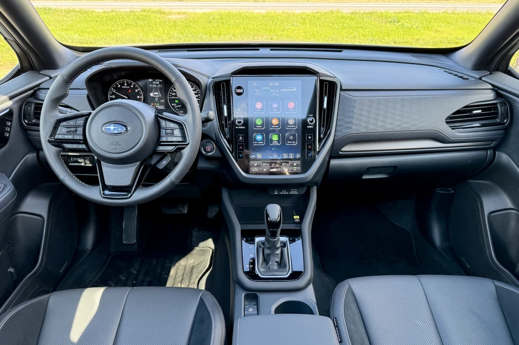Wnętrze samochodu osobowego Subaru, widoczny kokpit z nowoczesnym, dużym ekranem dotykowym na konsoli centralnej, kierownicą wielofunkcyjną oraz automatyczną skrzynią biegów, skórzane fotele i panele drzwiowe.