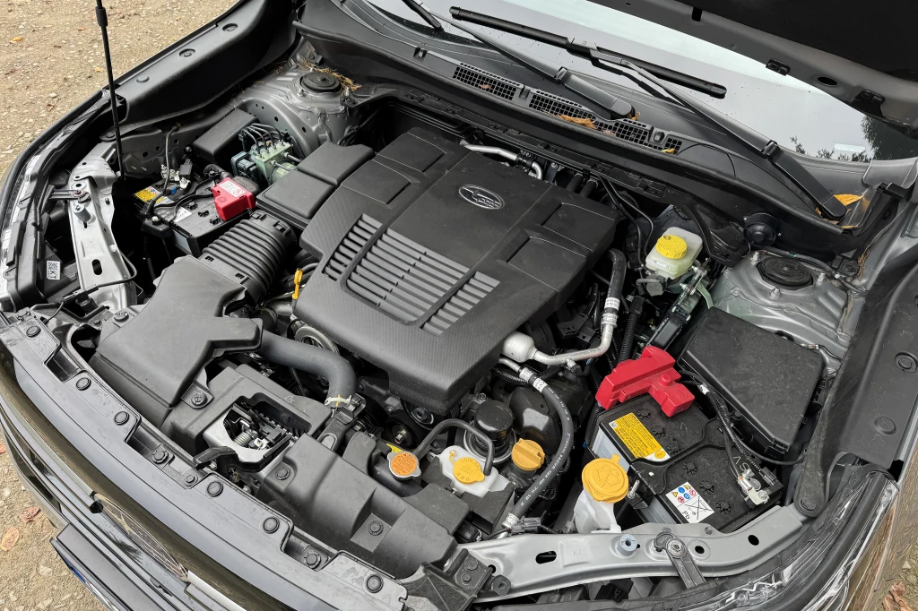 Komora silnika samochodu z wyraźnie widocznymi elementami technicznymi, takimi jak akumulator, przewody, zbiorniczki płynu oraz centralnie umieszczony duży plastikowy osłonięty silnik.