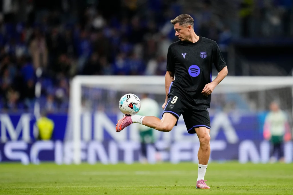 Robert Lewandowski Piłkarz w czarnej koszulce z numerem 9 wykonujący techniczną żonglerkę piłką na boisku podczas rozgrzewki. W tle zamazana widownia i niebiesko-białe banery.