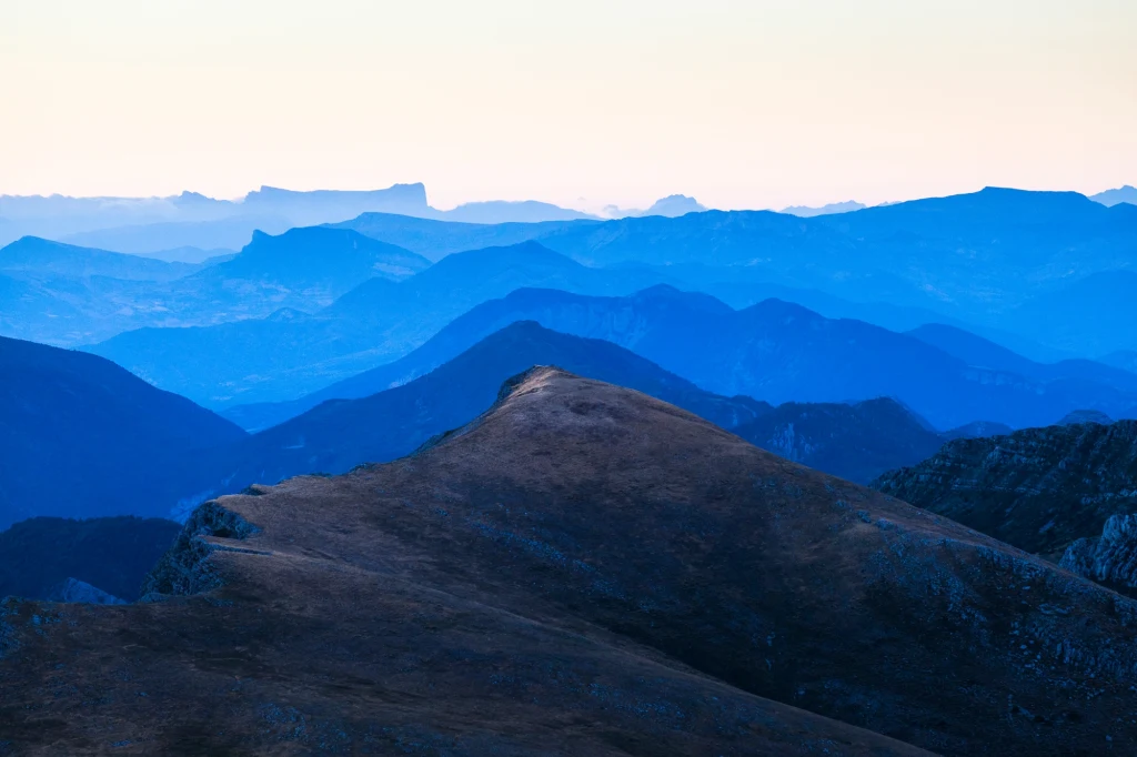 Wiele lodowców na całym świecie gwałtownie topnieje Pasmo górskie rozciągające się przez kilka planów, podkreślone różnymi odcieniami błękitu, tworząc efekt głębi, na pierwszym planie wyraźny grzbiet górski, w tle dalsze, zamglone szczyty.