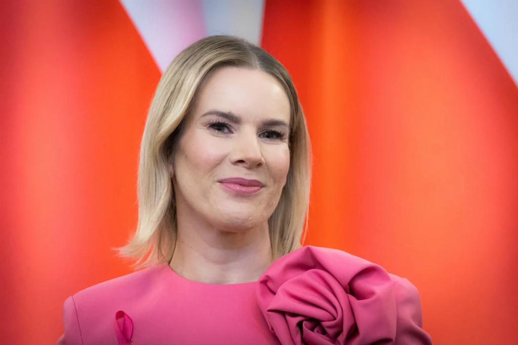 Pierwszy tego typu wywiad i pierwsza sesja okładkowa Marty Nawrockiej, otwierają nowy rozdział w jej zawodowym życiu Kobieta z blond włosami uśmiecha się, ubrana w różową suknię z dużą ozdobą w formie kwiatu na ramieniu, w tle czerwono-białe elementy geometryczne.