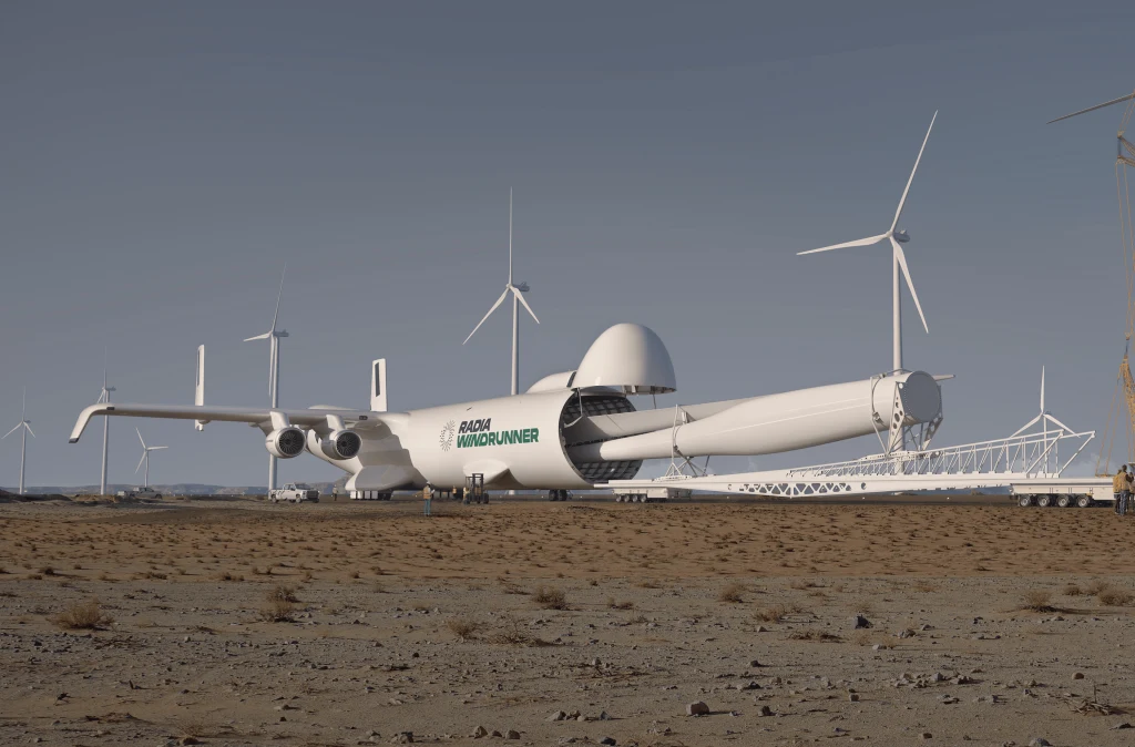 Radia Windrunner ma pozwolić na transport ładunków o długości ponad 100 metrów. Ogromny futurystyczny samolot transportowy z napisem Global Windrunner na kadłubie stoi na pustynnym podłożu w pobliżu dużych turbin wiatrowych, niebo jest czyste, a w tle widoczne są inne elementy infrastruktury energetycznej.