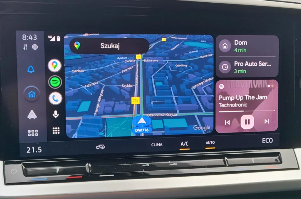 Ekran systemu multimedialnego samochodu z włączoną nawigacją Google, widokiem mapy miasta oraz listą skrótów do nawigacji do domu, serwisu i odtwarzania muzyki z tytułem utworu i wykonawcą.
