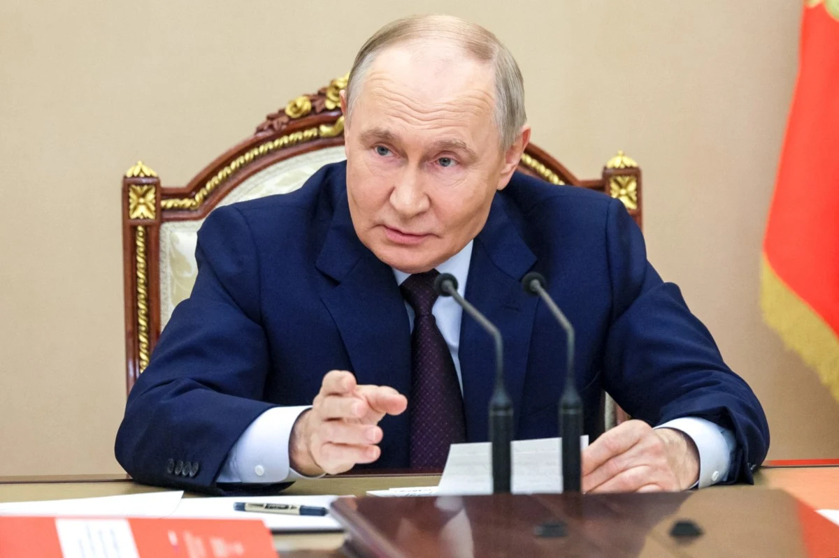 Władimir Putin reaguje na słowa Donalda Trumpa Siedzący przy stole mężczyzna w garniturze z dokumentem w dłoni, zwrócony ku rozmówcom, przed nim mikrofony, w tle fragment ozdobnego fotela i flagi.