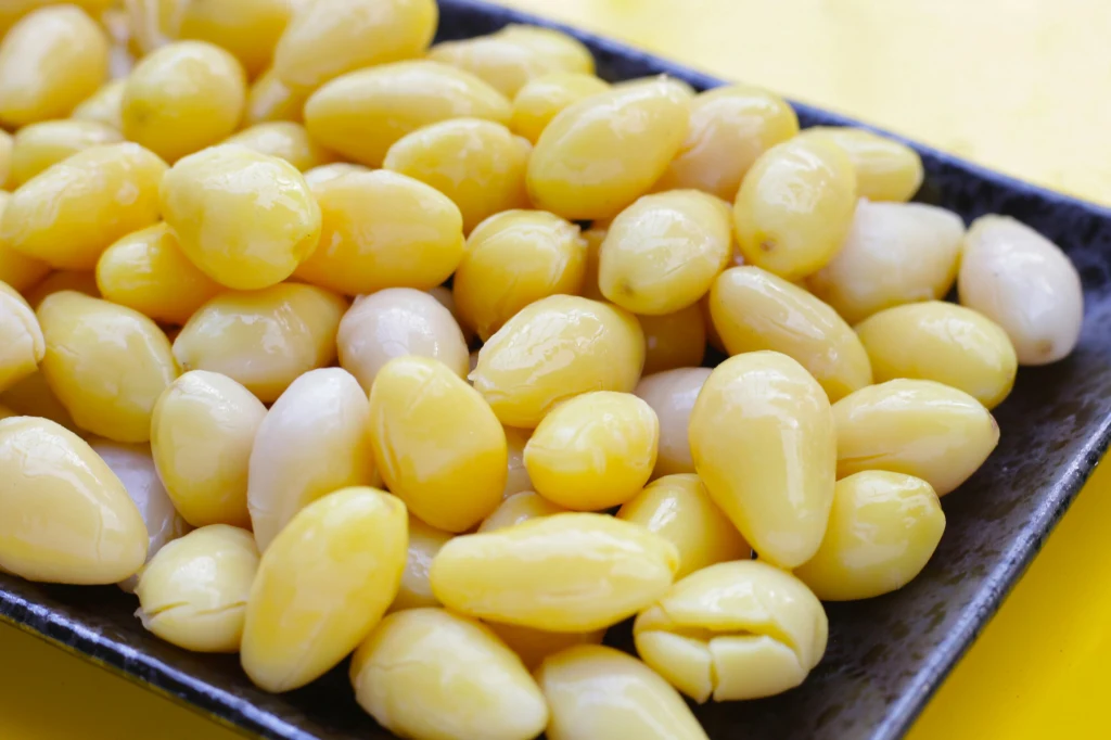 Smakowite orzeszki miłorzębu Duża ilość jasnożółtych nasion miłorzębu ginkgo ułożonych na czarnym prostokątnym talerzu, widocznych z bliska na żółtym tle.