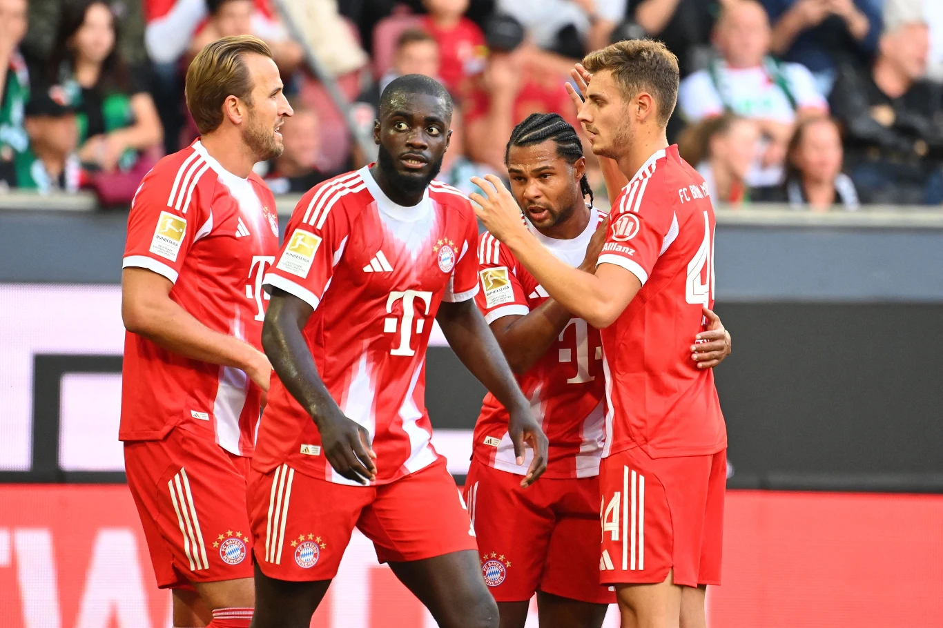 Dayot Upamecano (drugi z lewej) może już niebawem stać się zawodnikiem Realu Madryt Czterech piłkarzy Bayernu Monachium w czerwono-białych strojach podczas meczu, celebrujący wspólnie udaną akcję na tle trybun wypełnionych kibicami.