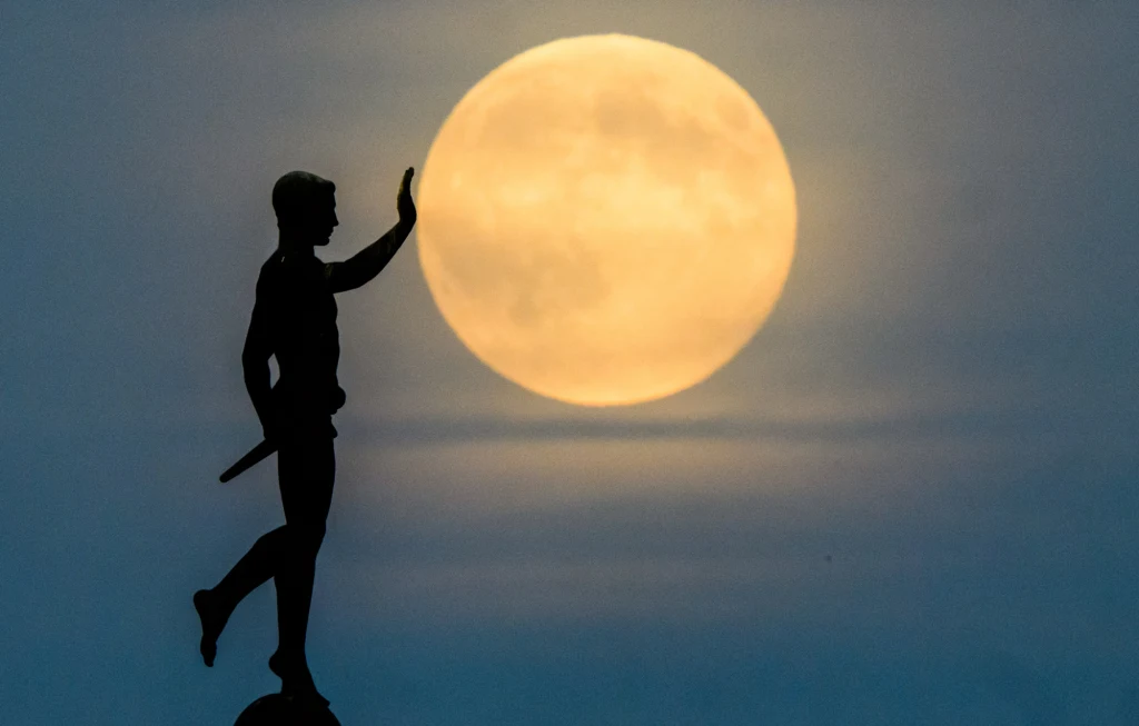 W nocy z środy na czwartek Księżyc znajdzie się w superpełni Czarna sylwetka posągu mężczyzny z ręką uniesioną w geście powitania lub zatrzymania, ustawiona na tle pełni księżyca na niebieskim niebie.