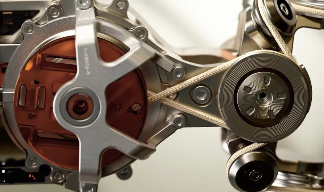 Skomplikowany mechanizm z widocznymi metalowymi elementami, paskami napędowymi oraz okrągłymi tarczami, całość tworzy nowoczesną i precyzyjną konstrukcję.