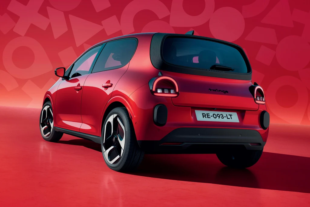 Nowe Renault Twingo E-Tech napędza silnik o mocy 82 KM Czerwony kompaktowy samochód osobowy o nowoczesnym designie, sfotografowany od tyłu na tle graficznego czerwonego tła z geometrycznymi wzorami. Tablica rejestracyjna pojazdu jest wyraźnie widoczna.