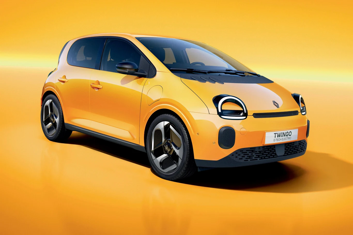 Nowoczesny, pomarańczowy samochód miejski Renault Twingo stoi na jednolitym, pomarańczowym tle. Pojazd ma kompaktową sylwetkę, aerodynamiczne linie oraz charakterystyczny kształt reflektorów.
