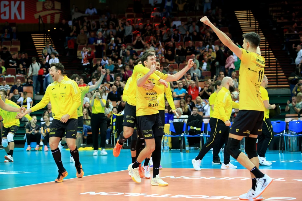 Siatkarze Bogdanki LUK Lublin i Stephane Antiga mogli świętować Grupa siatkarzy ubranych w żółte koszulki celebruje zwycięstwo na boisku, unosząc ręce w górę i wyrażając radość, w tle widać publiczność na trybunach.