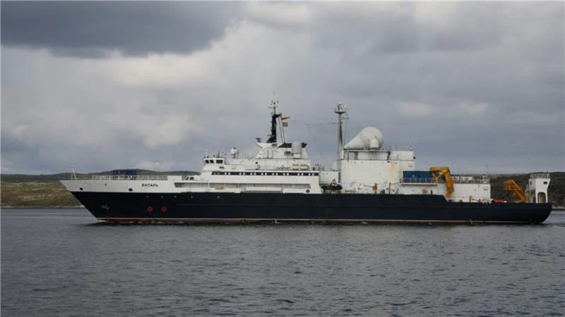 Rosyjski statek Jantar wszedł do służby w 2015 roku Duży, nowoczesny statek wyposażony w różnorodne anteny, sprzęt komunikacyjny i rozbudowane systemy na pokładzie, płynący w spokojnych wodach przy pochmurnym niebie. Tło stanowi niska linia brzegowa.