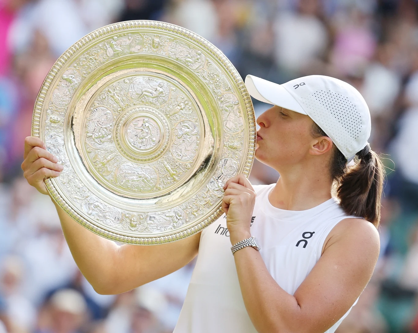 Iga Świątek z trofeum za wygraną w Wimbledonie Tenisistka ubrana na biało całuje duże srebrne trofeum, wyrażając radość i dumę ze zdobycia nagrody podczas ważnego turnieju tenisowego.