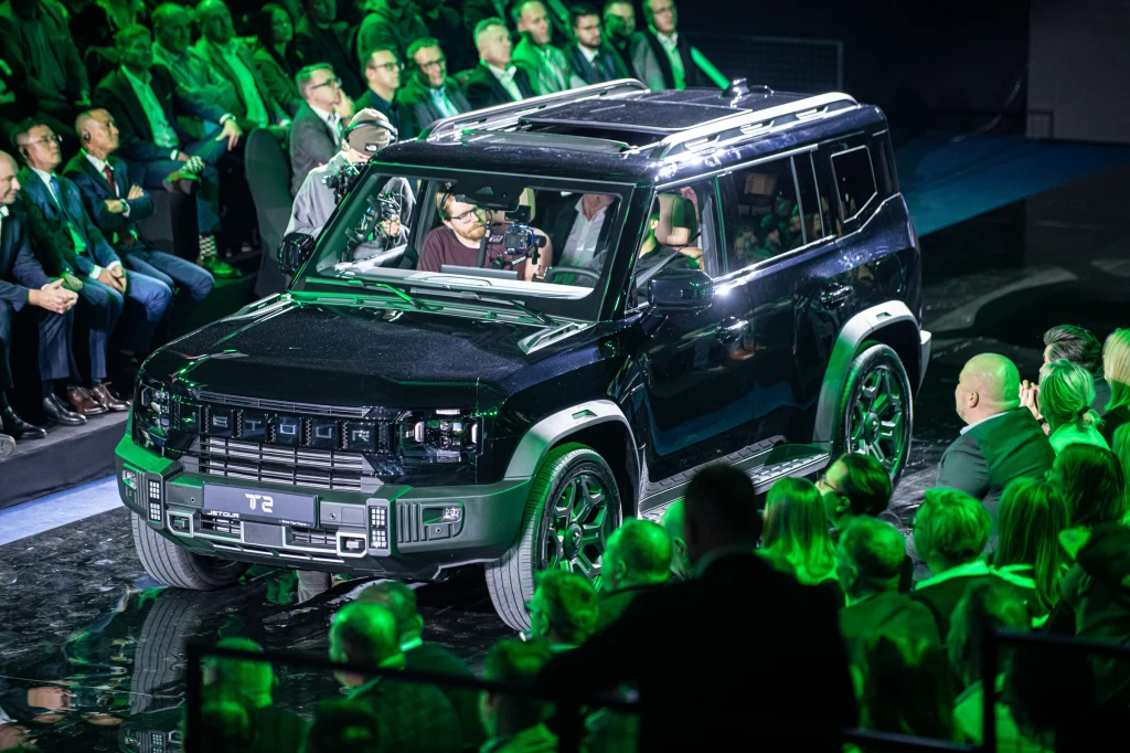 Jetour T2 Luksusowy czarny samochód terenowy prezentowany na scenie przed licznie zgromadzoną publicznością, uczestnicy wydarzenia obserwują pojazd w oświetleniu sceny utrzymanym w zielonej tonacji.