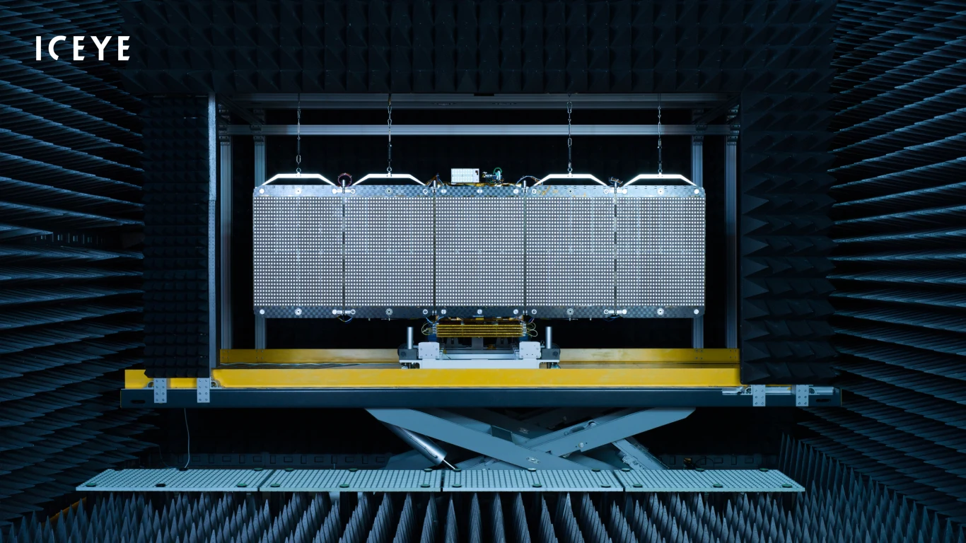 Panele technologiczne umieszczone w komorze bezodbiciowej, otoczone piankami absorbującymi fale, przygotowane do testów lub badań laboratoryjnych, logotyp ICEYE w lewym górnym rogu.