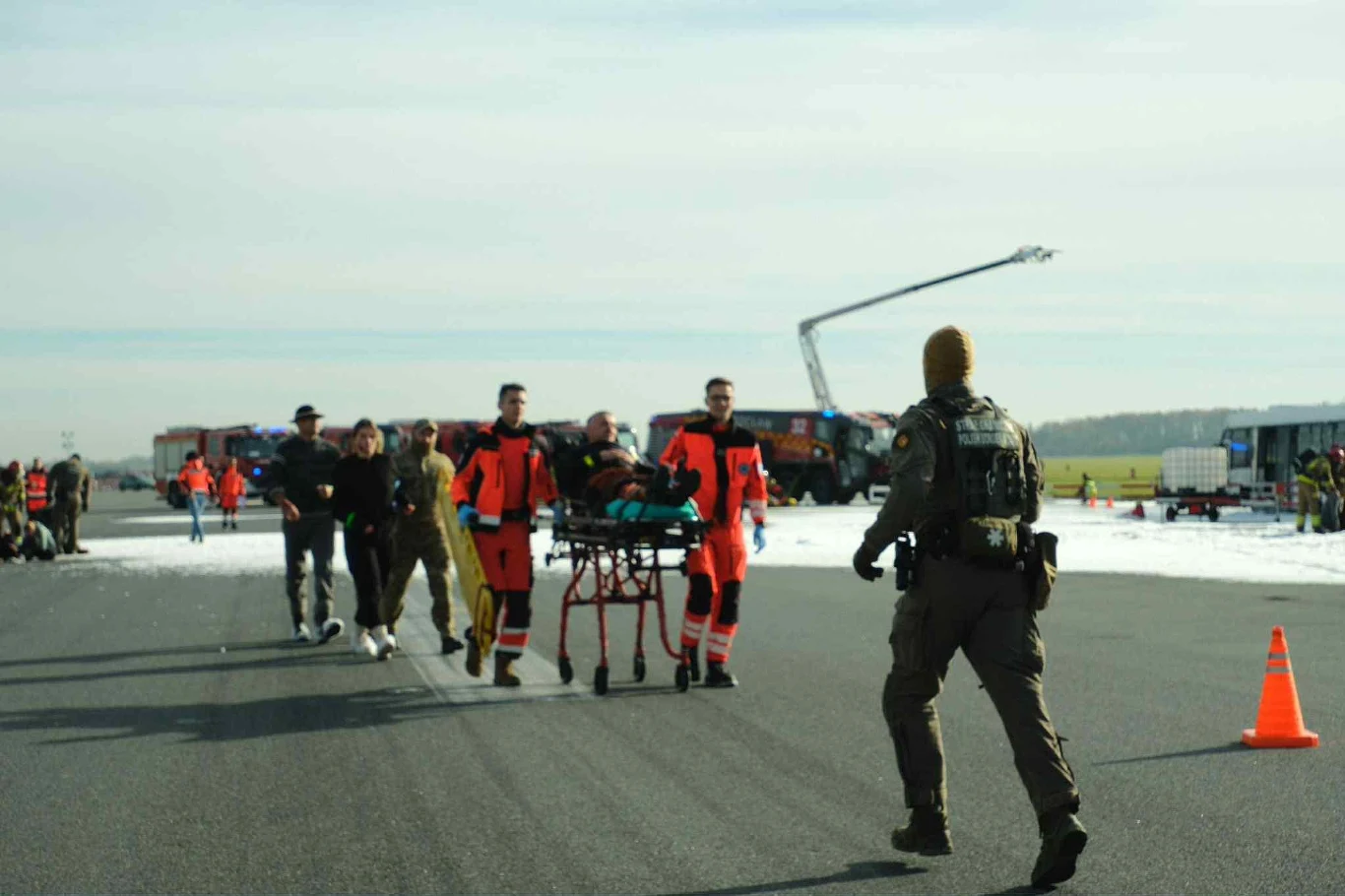 Ćwiczenia NOKIA25 Ratownicy medyczni i służby mundurowe transportują osobę na noszach po pasie lotniska, wokół rozstawione są wozy strażackie oraz zabezpieczenia.