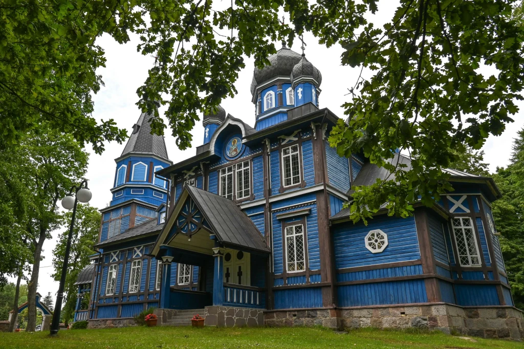 Cerkiew w Puchłach to najpiękniejsza świątynia prawosławna na Podlasiu Drewniana cerkiew w stylu rosyjskim z niebieskimi ścianami, strzelistymi wieżami zakończonymi cebulastymi kopułami, białymi okiennicami oraz bogatymi zdobieniami, otoczona zielonymi drzewami i bujną trawą.