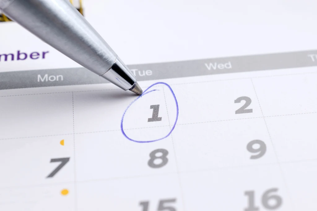 Jak planować urlop w 2026 roku, by wykorzystać ustawowo dni wolne od pracy? Srebrny długopis wskazuje datę pierwszego dnia miesiąca zaznaczoną niebieskim okręgiem na papierowym kalendarzu.