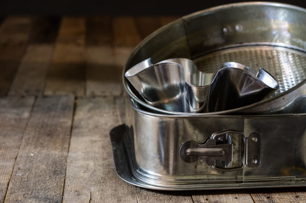 Blachy do pieczenia ciast mają mnóstwo zakamarków Metalowe foremki do pieczenia w różnych kształtach ustawione na drewnianym blacie, widoczne detale zamka w największej formie.