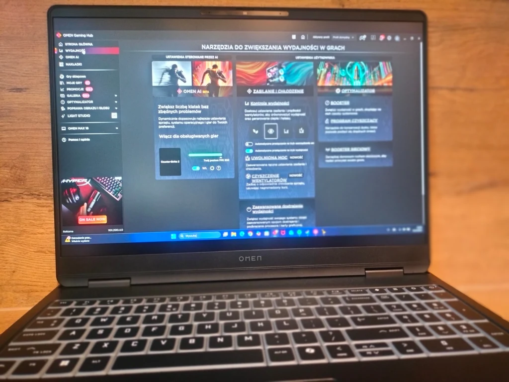 OMEN MAX 16 Laptop HP Omen z włączonym oprogramowaniem do optymalizacji wydajności w grach, wyraźnie widoczny ekran komputera z interfejsem użytkownika, klawiatura podświetlana, tło drewniane.