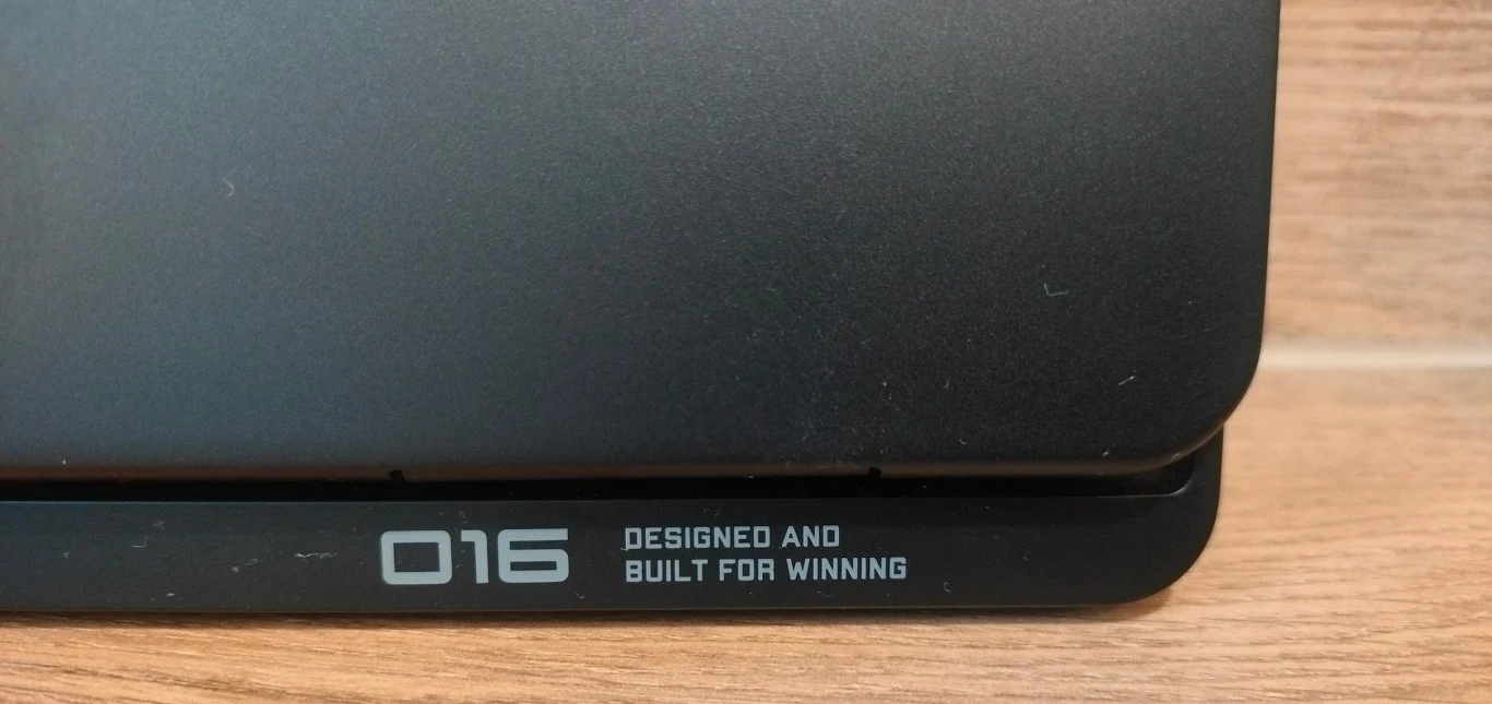 Fragment czarnej obudowy z widocznym napisem '016 Designed and built for winning' na tle drewnianego podłoża.