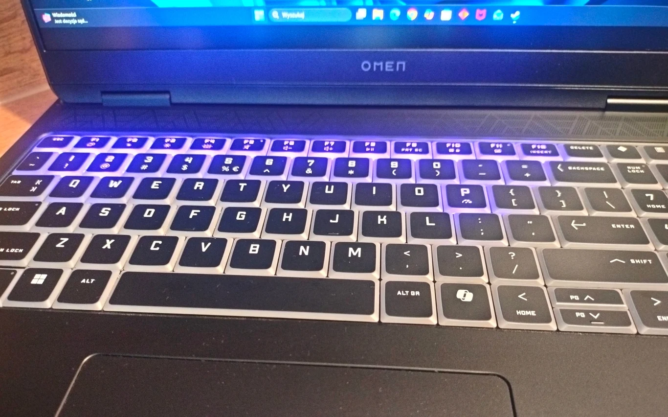 Klawiatura laptopa marki Omen z częściowo widocznym ekranem i podświetleniem klawiszy na fioletowo-niebiesko.