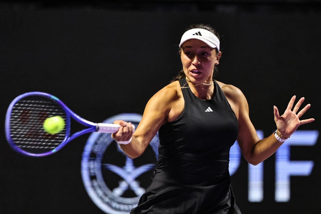 Tenisistka w czarnym stroju sportowym odbijająca piłkę podczas meczu, z wyraźnym napięciem na twarzy, dynamiczne ujęcie podkreślające ruch rakietą i skupienie zawodniczki.