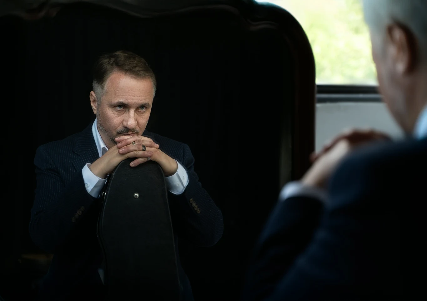 Rico Schett wydał solowy debiut "Fair Trade" Mężczyzna w garniturze oparty o futerał do gitary, patrzący zadumanym wzrokiem w lustro, w którym odbija się fragment jego sylwetki.