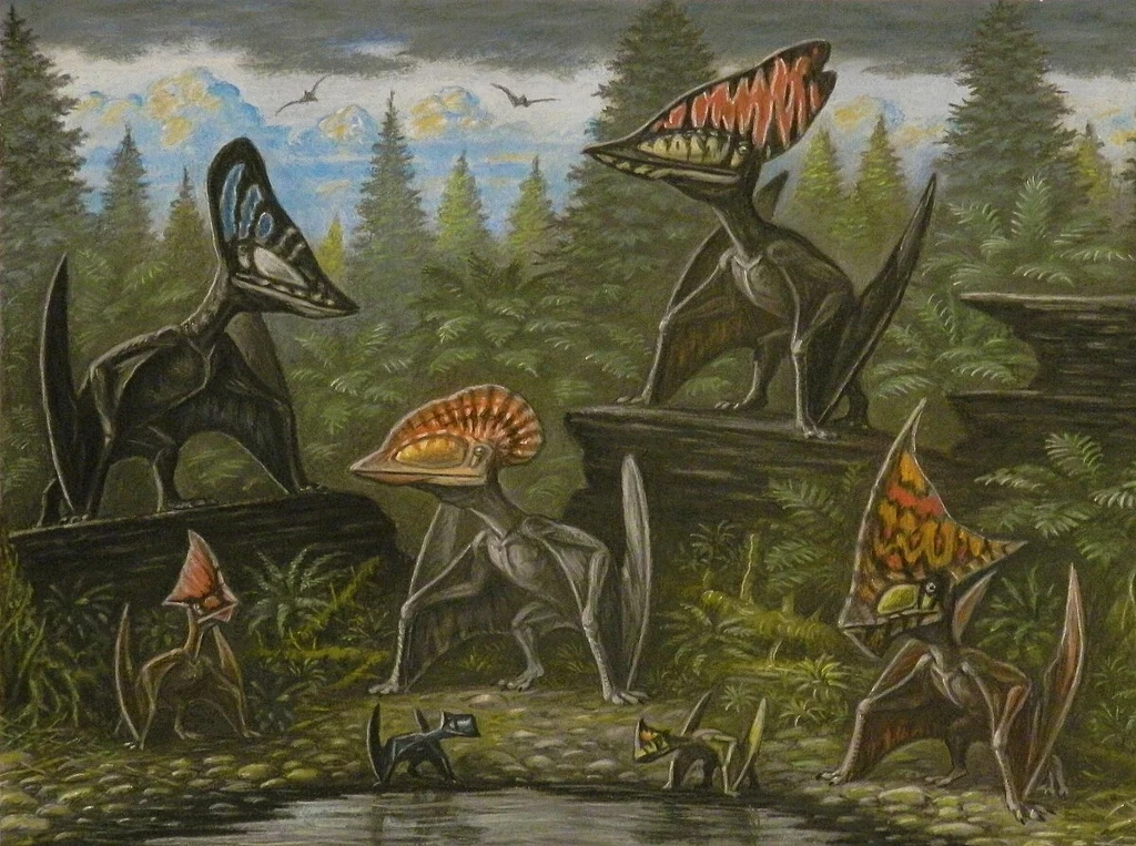 Grupa pterozaurów o kolorowych grzebieniach na głowach zgromadzona wśród roślinności prehistorycznego lasu, nad wodą; w tle widoczne są drzewa iglaste oraz lecące w powietrzu mniejsze pterozaury na tle nieba.