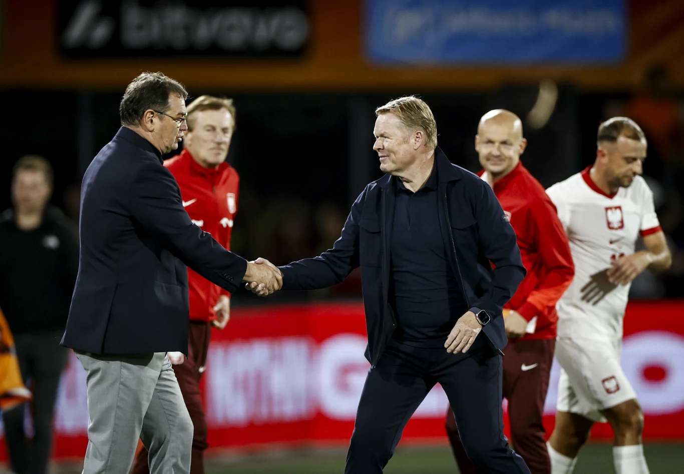 Jan Urban i Ronald Koeman, 04.09.2025 r. Dwaj trenerzy wymieniają uścisk dłoni na boisku, w tle kilka osób w sportowych strojach reprezentujących Polskę na wydarzeniu piłkarskim, atmosfera rywalizacji i sportowego szacunku.