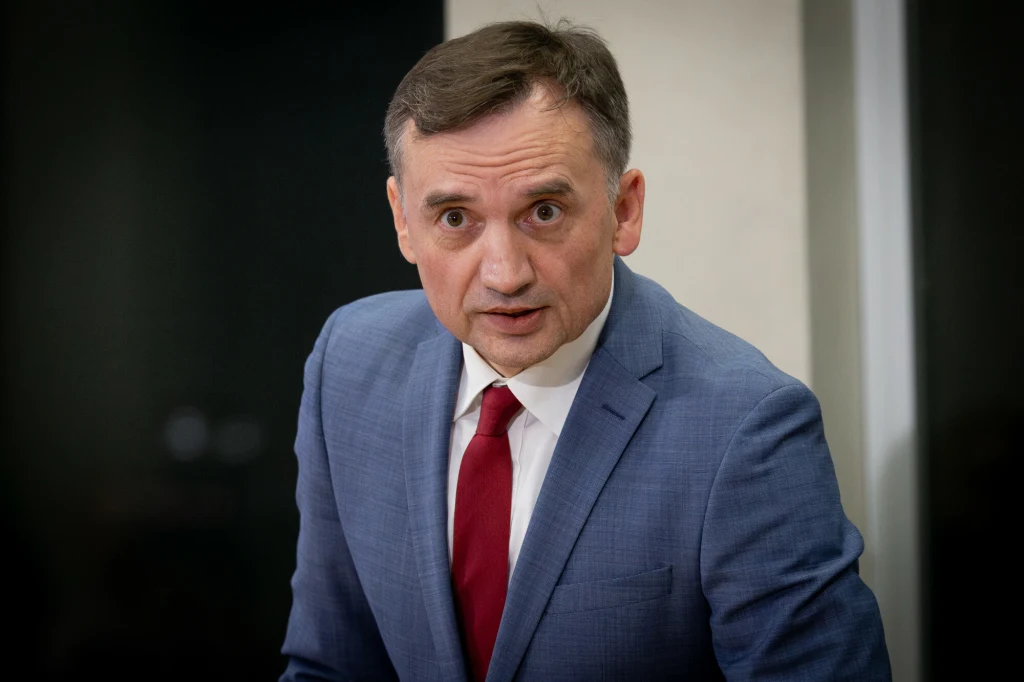 Zbigniew Ziobro udzielił wywiadu przed głosowaniem nad jego immunitetem Mężczyzna w średnim wieku w niebieskim garniturze i czerwonym krawacie, stoi na tle jasnej ściany, patrzy z powagą w stronę obiektywu.