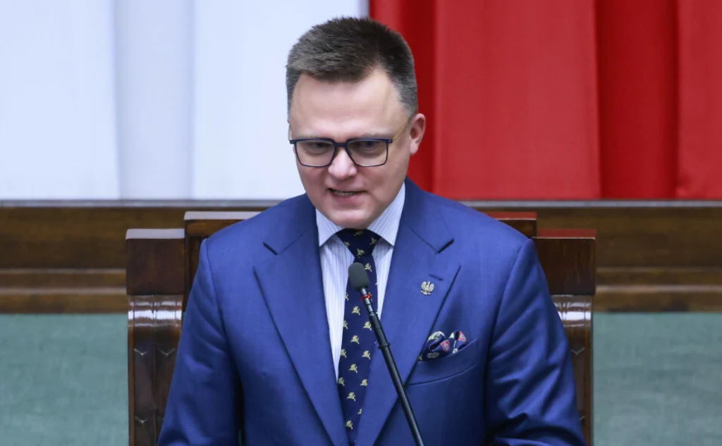 Szymon Hołownia w trakcie 44. posiedzenia Sejmu podziękował posłom za ostatnie dwa lata Mężczyzna w niebieskim garniturze i okularach przemawia przy mównicy, w tle widoczne polskie barwy narodowe.