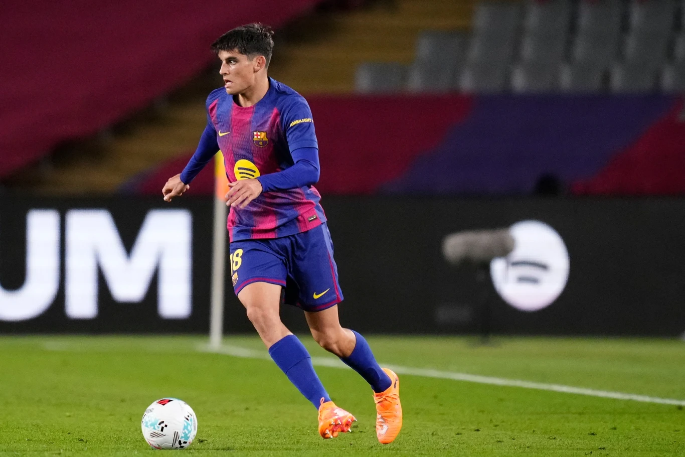 Piłkarz w barwach FC Barcelony kontroluje piłkę podczas meczu na stadionie. W tle widoczna trybuna oraz fragmenty murawy.