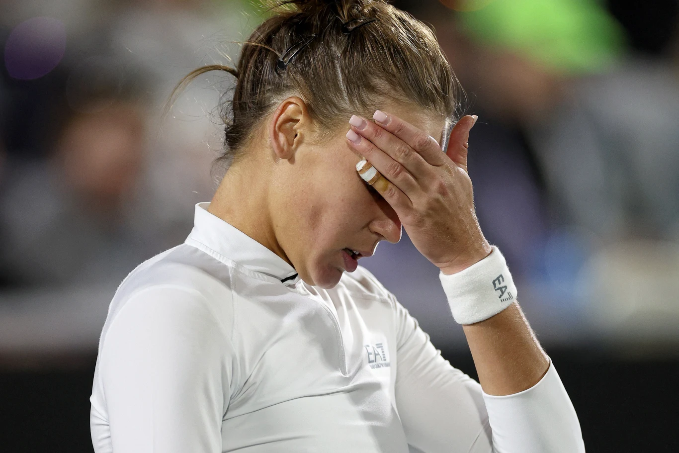 Weronika Kudiermietowa pewnie wciąż nie dowierza w to, co wydarzyło się w półfinale WTA Finals 2025 Sportowiec ubrana w białą koszulkę zasłania twarz dłonią, wyrażając emocje związane z rywalizacją. Jej włosy są związane, a tło jest rozmyte, co podkreśla skupienie na postaci.