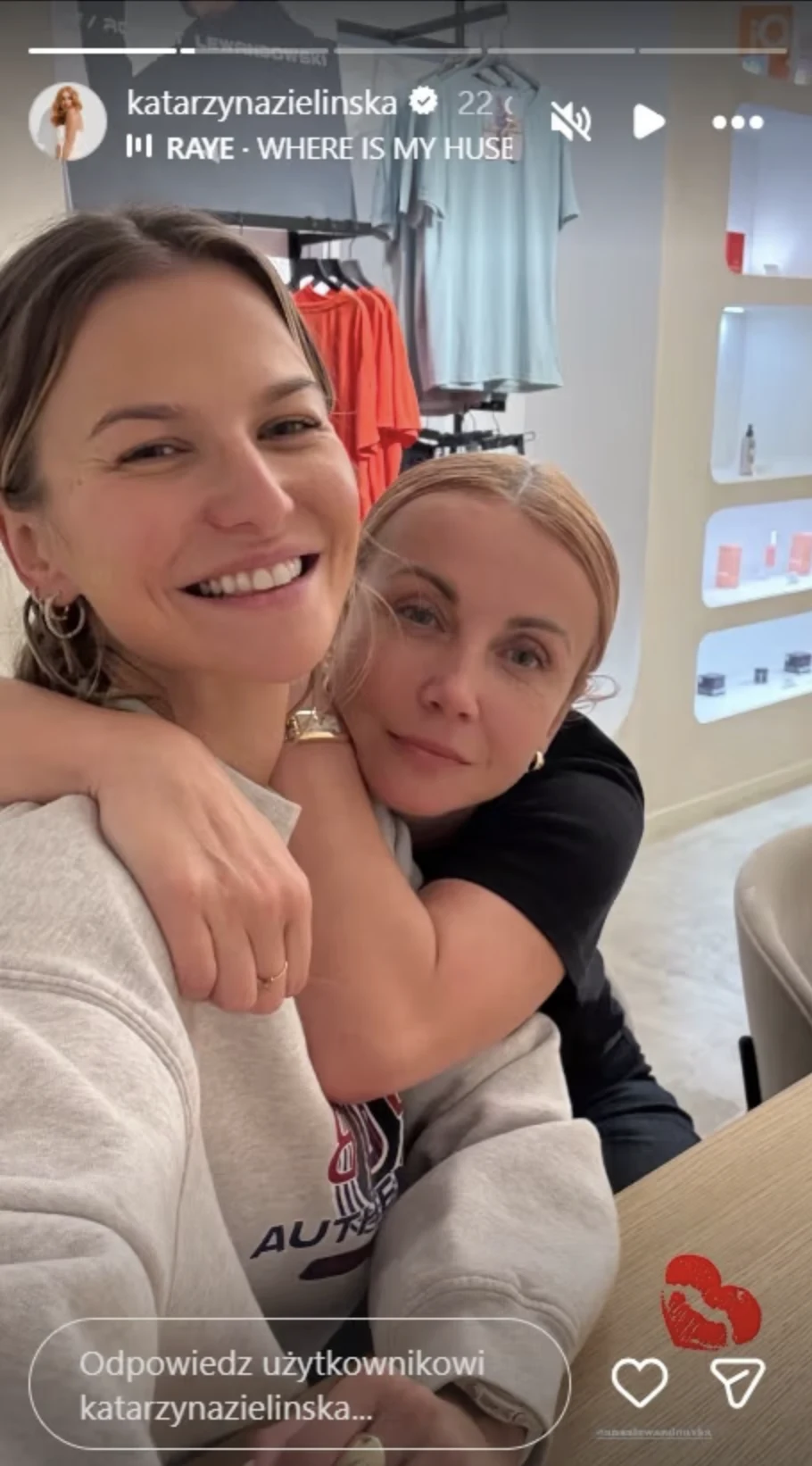 Katarzyna Zielińska odwiedziła Edan Studios Anny Lewandowskiej Dwie kobiety obejmujące się z uśmiechem przy stole we wnętrzu sklepu lub salonu, w tle regał z kolorowymi ubraniami i półkami.