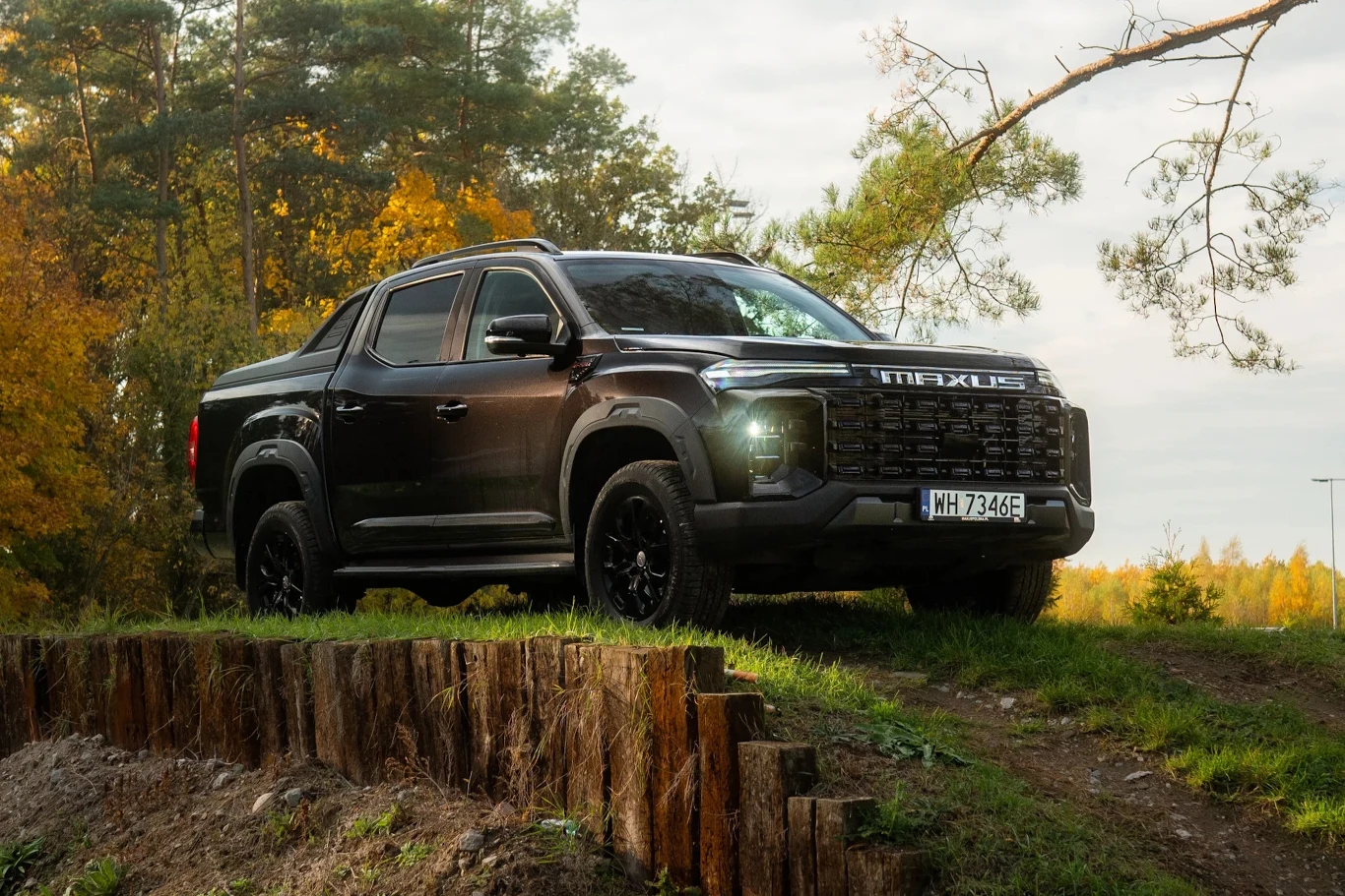Maxus T60 MAX to jedna z najciekawszych pozycji na rynku pick-upów w Polsce Czarny pickup marki Maxus stoi na wzniesieniu w lesie, otoczony drzewami w jesiennych kolorach, podkreślając możliwości terenowe pojazdu.