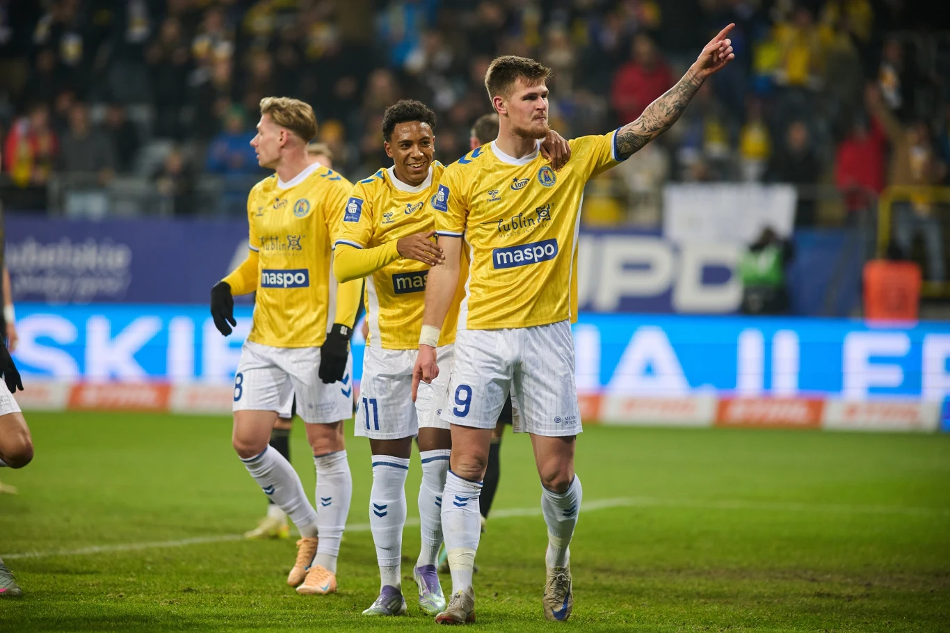 Motor Lublin Grupa piłkarzy w żółtych koszulkach świętuje zdobycie bramki podczas meczu, jeden z zawodników z numerem 9 wskazuje palcem w stronę trybun, a pozostali podążają za nim z radością na twarzach.