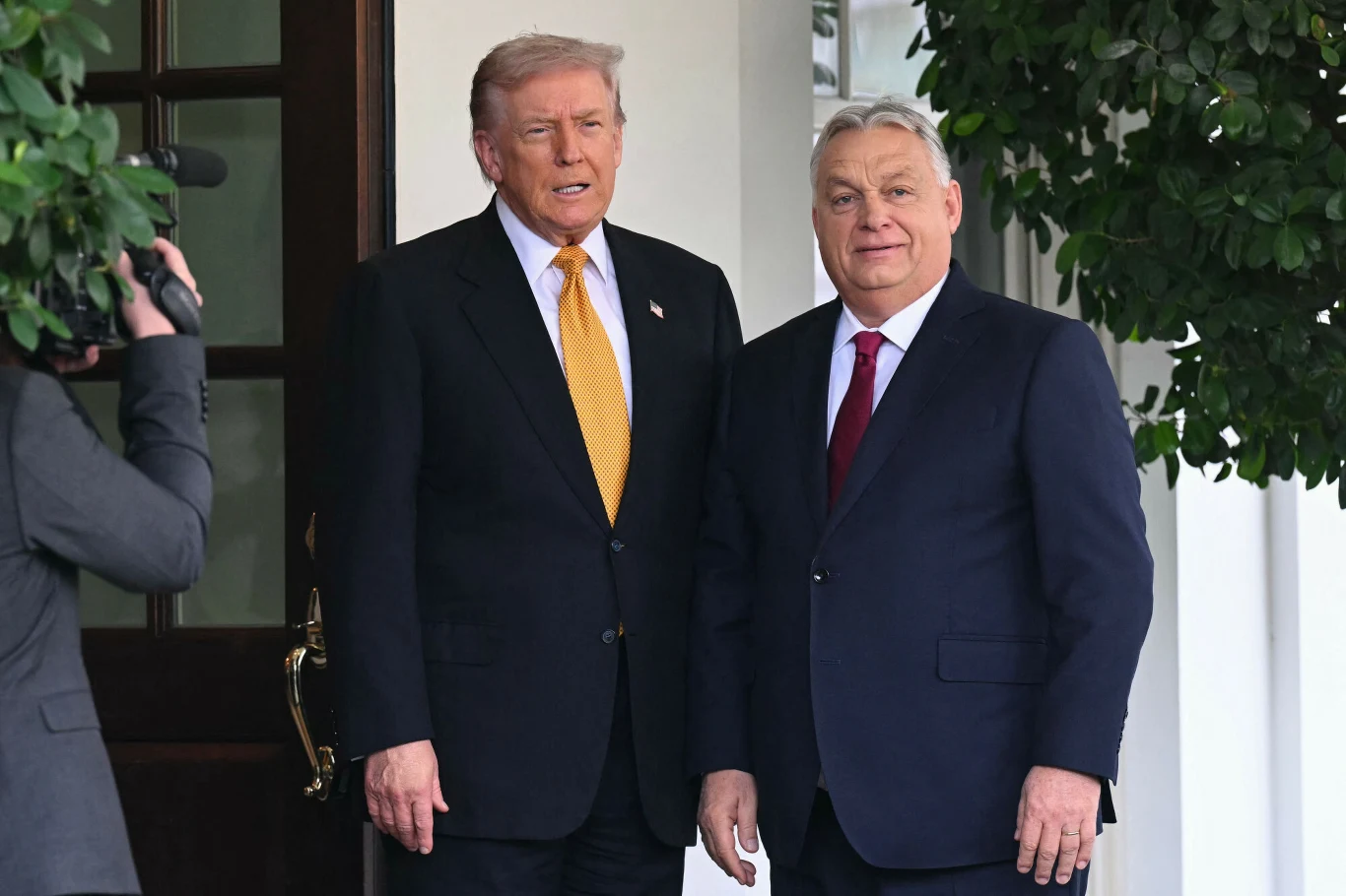 "Polityczne zwycięstwo Orbana". Media ujawniają prawdę ws. sankcji od USA (zdj. ilustracyjne) Dwóch mężczyzn w garniturach stoi obok siebie na tle drzwi wejściowych i zieleni. Jeden z nich ma żółty krawat, a drugi czerwony. W tle widoczna osoba z kamerą.