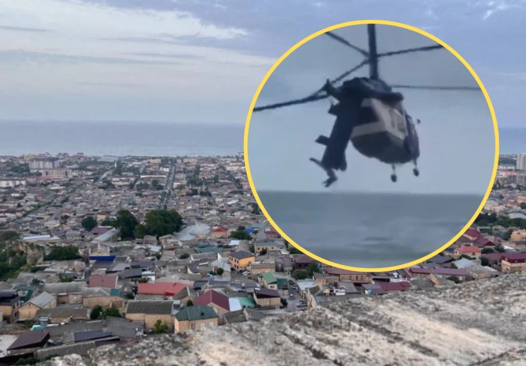 Rosja. Katastrofa helikoptera w Dagestanie. Nie żyje pięć osób Panorama miasta z widoczną zabudową mieszkalną oraz fragmentem wybrzeża. W okrągłym zbliżeniu widoczny wojskowy helikopter unoszący się nad wodą lub wybrzeżem.