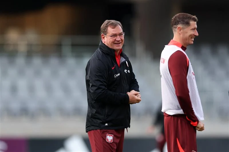 Dwóch mężczyzn w strojach sportowych reprezentacji Polski podczas treningu na stadionie, jeden z nich uśmiechnięty, w tle rozmyte trybuny.