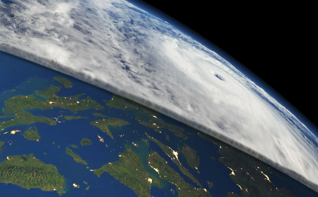 Fragment powierzchni Ziemi pokryty zielonymi wyspami i błękitnymi wodami, nad którym rozciągają się gęste chmury oraz wyraźnie widoczny owal oka cyklonu.