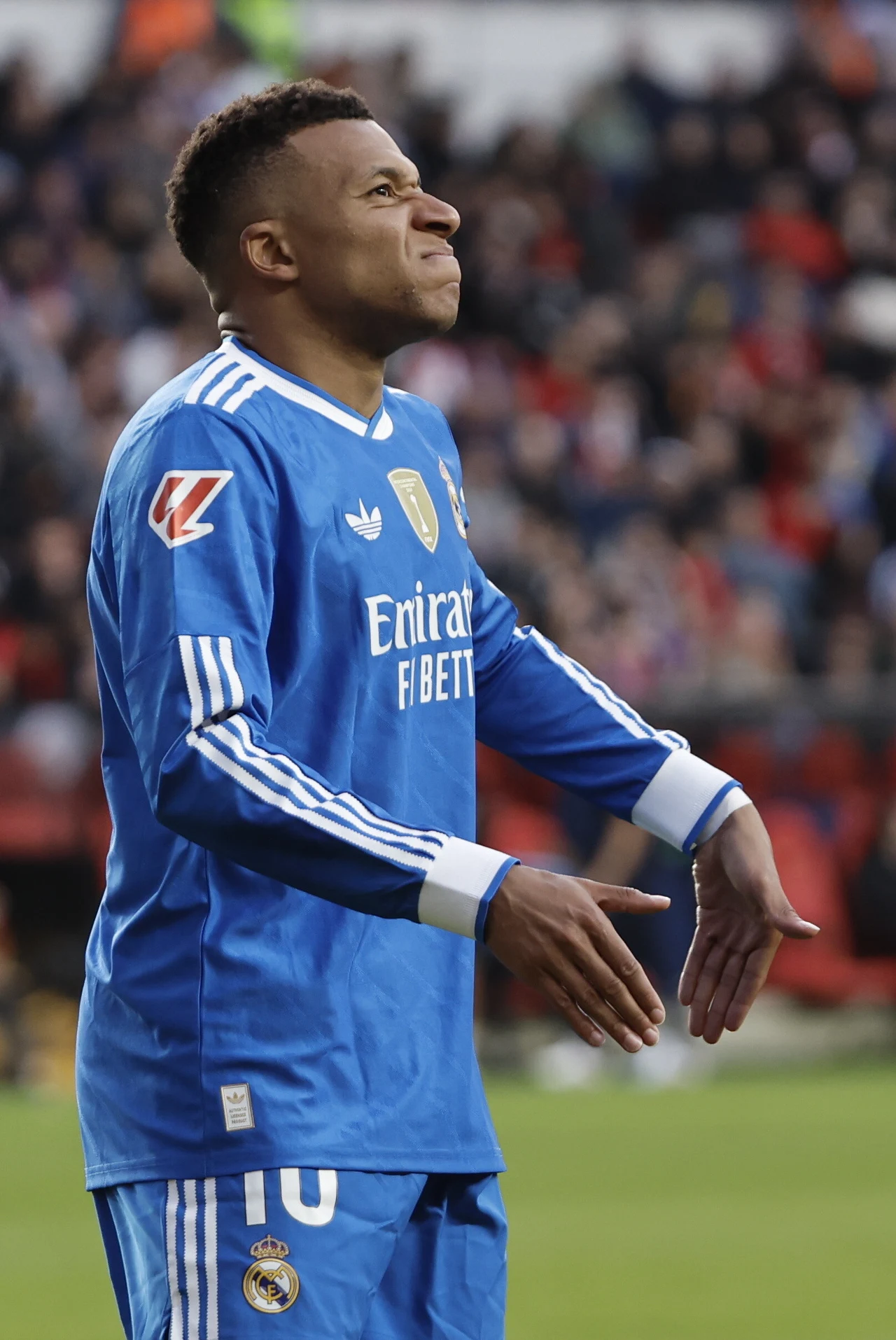 Piłkarz w niebieskim stroju Realu Madryt wykonuje charakterystyczny gest podczas meczu, na tle trybun wypełnionych kibicami.