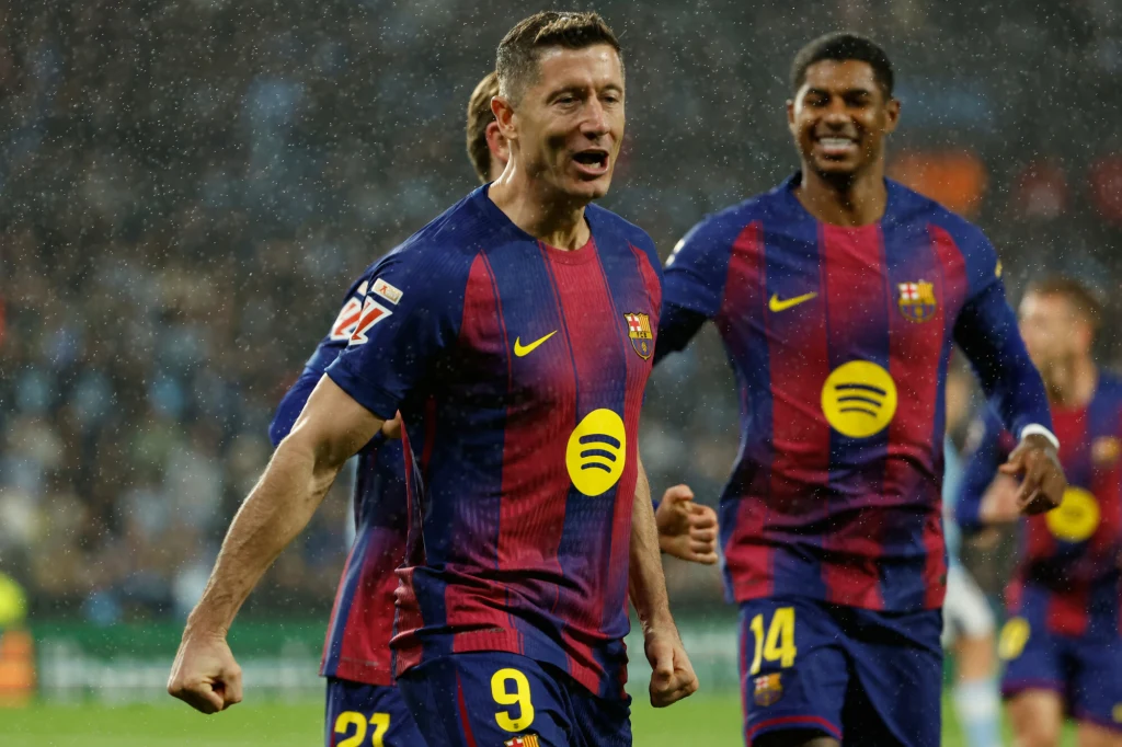 Robert Lewandowski Piłkarz drużyny FC Barcelona w granatowo-bordowej koszulce z numerem 9 na pierwszym planie świętuje sukces na boisku, towarzyszą mu uśmiechnięci koledzy z drużyny w tle.